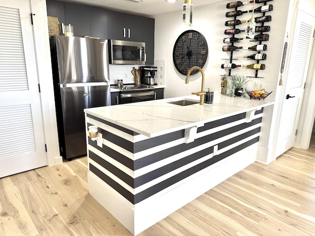 kitchen featuring appliances with stainless steel finishes, light wood-style floors, a sink, dark cabinetry, and a peninsula