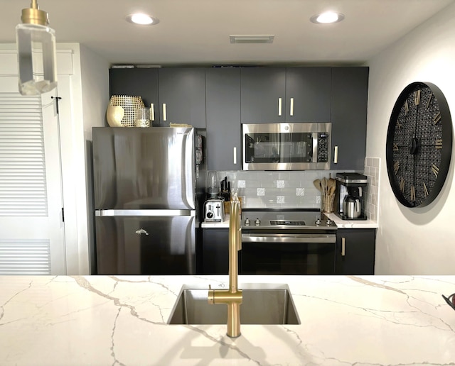 kitchen featuring light stone counters, backsplash, gray cabinets, stainless steel appliances, and a sink