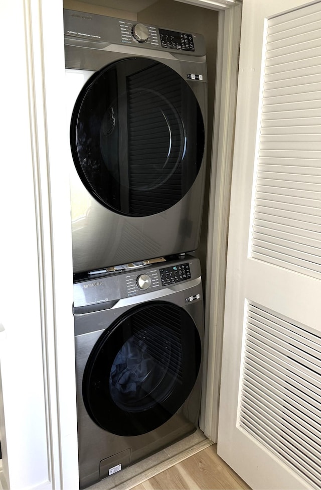 washroom with stacked washer and dryer, wood finished floors, and laundry area