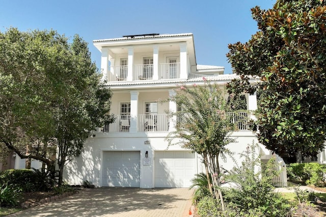 greek revival house featuring a garage, decorative driveway, a balcony, and stucco siding