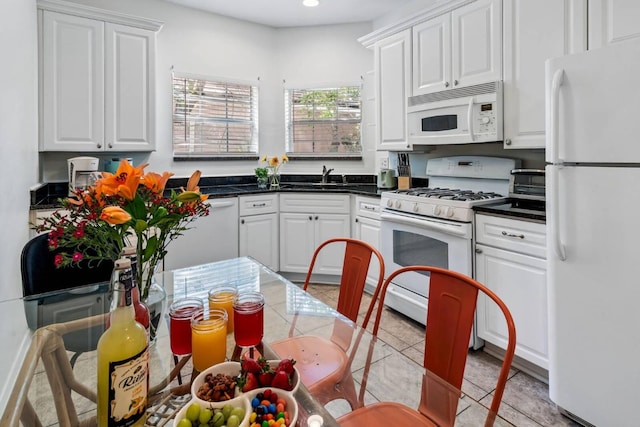 kitchen with light tile patterned floors, dark countertops, white cabinetry, a sink, and white appliances