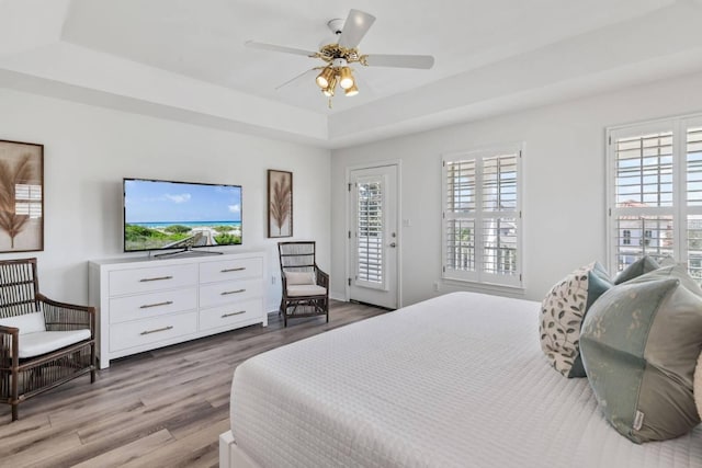 bedroom with access to exterior, a tray ceiling, multiple windows, and wood finished floors