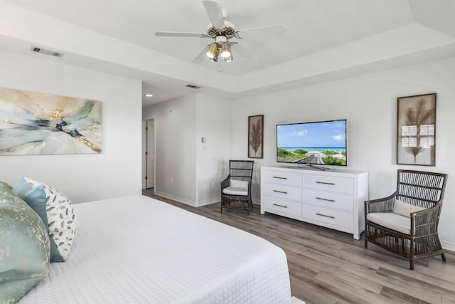 bedroom with a tray ceiling, wood finished floors, visible vents, and baseboards