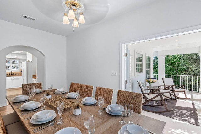 dining area with light wood-style floors, arched walkways, visible vents, and a ceiling fan