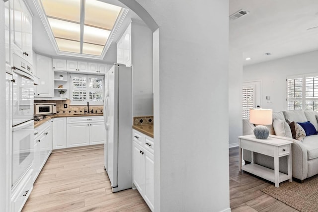 kitchen featuring arched walkways, visible vents, light wood-style floors, a sink, and white appliances