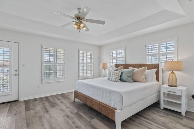 bedroom featuring light wood-type flooring, a tray ceiling, ceiling fan, and baseboards