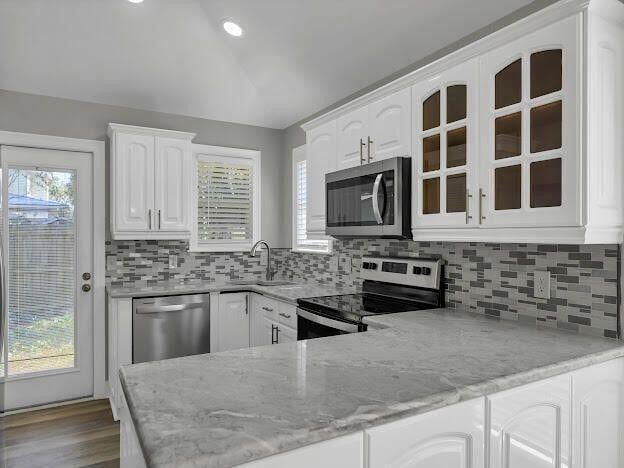 kitchen featuring lofted ceiling, appliances with stainless steel finishes, glass insert cabinets, white cabinetry, and a sink