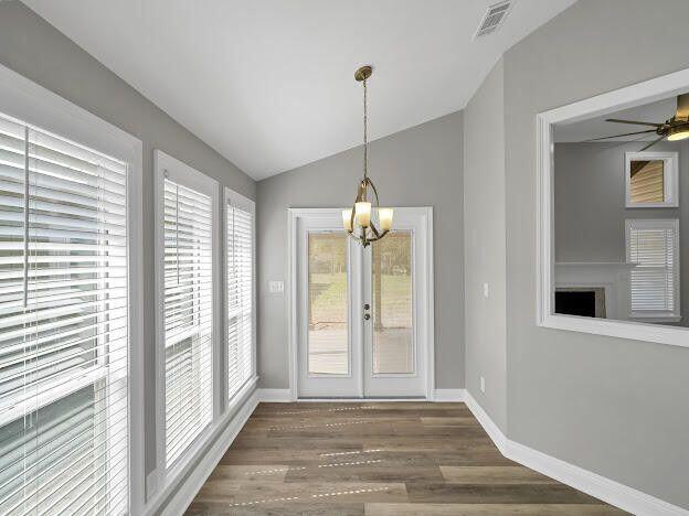 unfurnished dining area with lofted ceiling, visible vents, baseboards, and wood finished floors