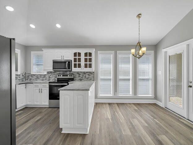 kitchen featuring stainless steel appliances, light countertops, backsplash, white cabinetry, and wood finished floors