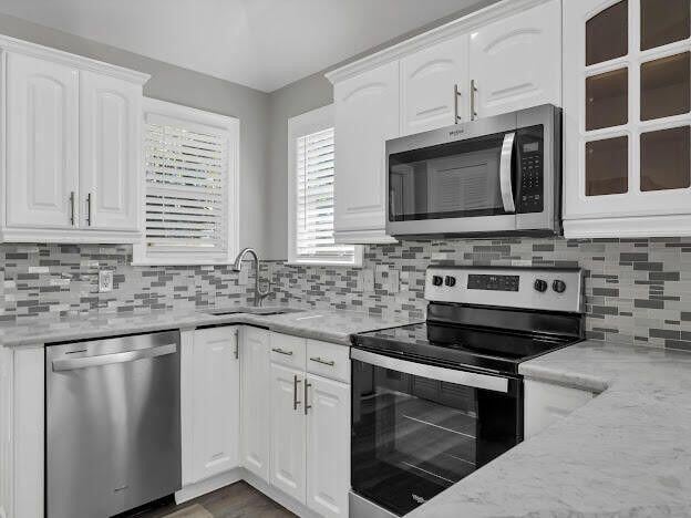 kitchen featuring light stone countertops, white cabinetry, appliances with stainless steel finishes, and a sink