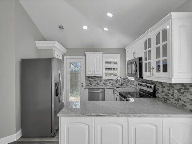 kitchen with decorative backsplash, appliances with stainless steel finishes, glass insert cabinets, a peninsula, and a sink