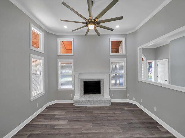 unfurnished living room featuring a fireplace, wood finished floors, a ceiling fan, baseboards, and ornamental molding