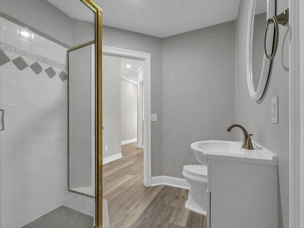 bathroom with toilet, vanity, a shower stall, wood finished floors, and baseboards