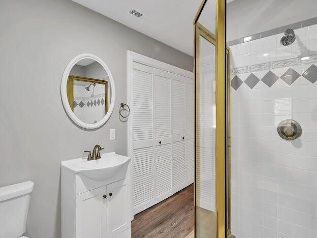 bathroom featuring visible vents, toilet, wood finished floors, a tile shower, and vanity