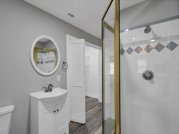 full bath featuring toilet, wood finished floors, vanity, visible vents, and tiled shower