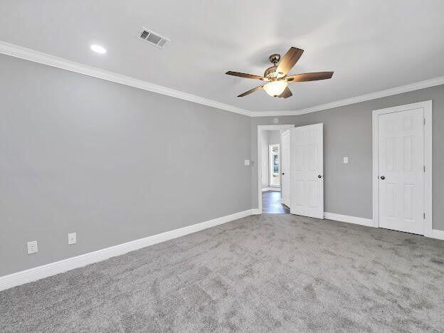 unfurnished bedroom featuring carpet, crown molding, visible vents, and baseboards