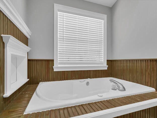 bathroom with wooden walls, wainscoting, a bath, and a healthy amount of sunlight