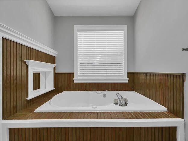 bathroom featuring a wainscoted wall and a bath