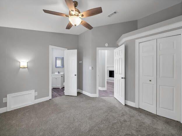 unfurnished bedroom with carpet floors, a closet, visible vents, ensuite bathroom, and baseboards