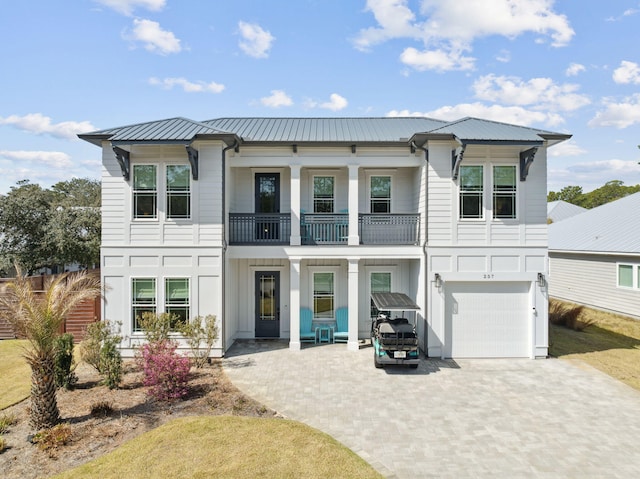 view of front of home with decorative driveway, an attached garage, board and batten siding, metal roof, and a balcony