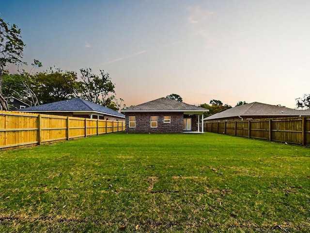 yard at dusk featuring a fenced backyard