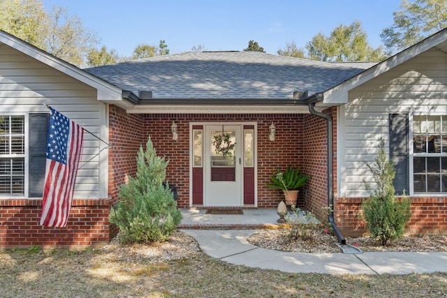 view of exterior entry featuring roof with shingles and brick siding