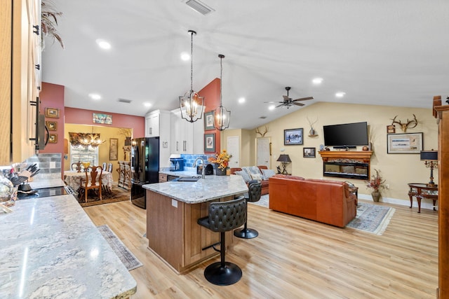 kitchen featuring a breakfast bar area, visible vents, freestanding refrigerator, a sink, and light stone countertops