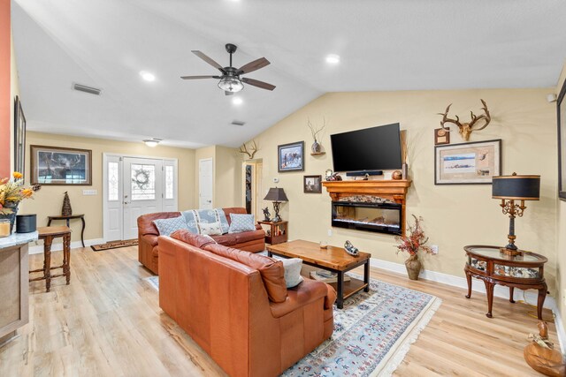 living area featuring light wood finished floors, baseboards, visible vents, a glass covered fireplace, and vaulted ceiling