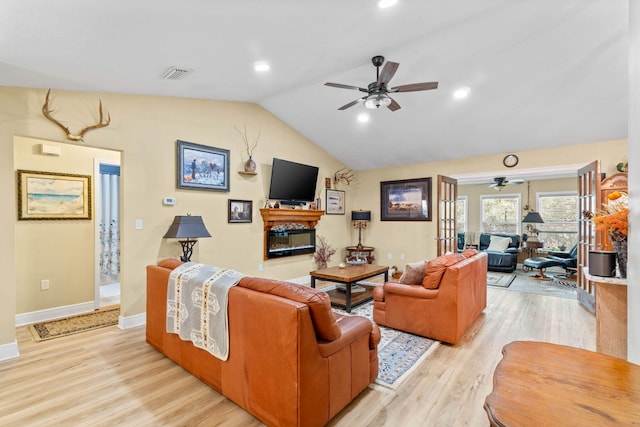 living room with lofted ceiling, light wood-style flooring, visible vents, and a glass covered fireplace