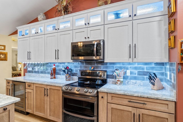 kitchen featuring beverage cooler, decorative backsplash, lofted ceiling, light stone counters, and stainless steel appliances