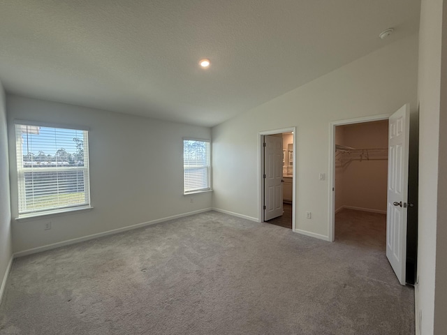 unfurnished bedroom featuring a walk in closet, a textured ceiling, carpet, baseboards, and vaulted ceiling