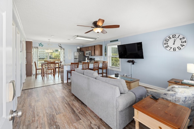 living room with ceiling fan, ornamental molding, baseboards, and light wood-style floors