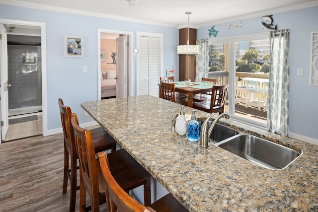 kitchen featuring baseboards, a breakfast bar area, ornamental molding, dark wood-type flooring, and a sink