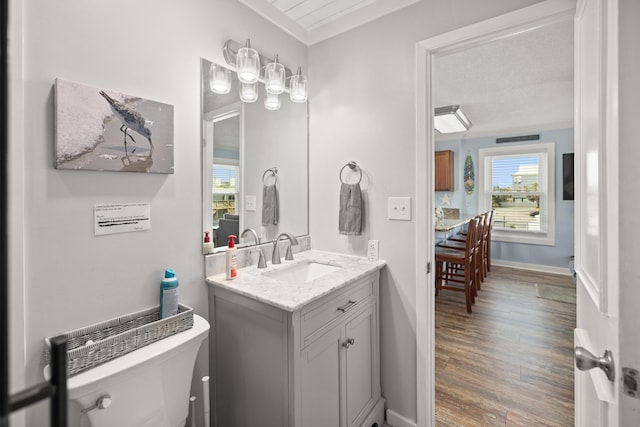 half bathroom featuring baseboards, toilet, ornamental molding, wood finished floors, and vanity