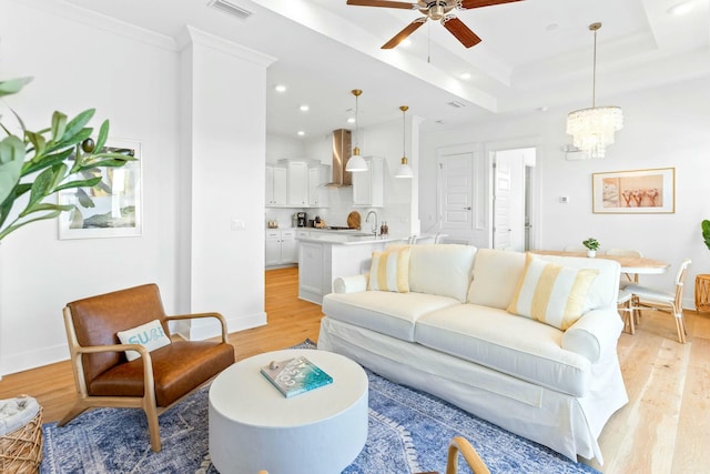 living area featuring light wood-type flooring, a tray ceiling, visible vents, and crown molding