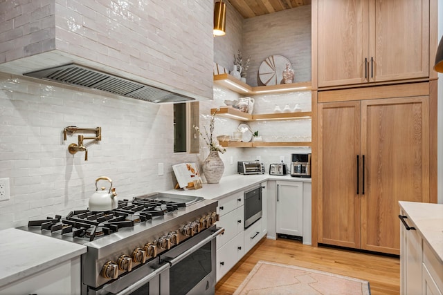 kitchen with range with two ovens, ventilation hood, light wood-type flooring, light stone countertops, and tasteful backsplash