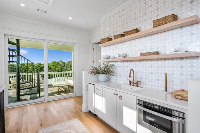 kitchen with a sink, light wood-style floors, ornamental molding, backsplash, and open shelves