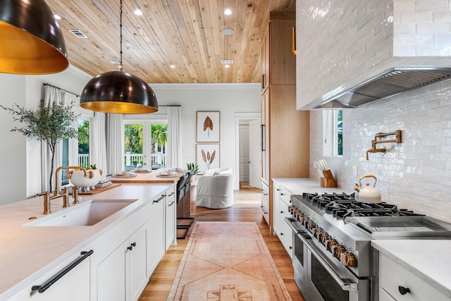 kitchen with range with two ovens, backsplash, a sink, wooden ceiling, and wall chimney exhaust hood