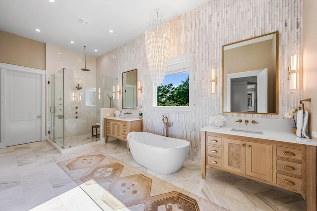 full bathroom featuring marble finish floor, two vanities, a freestanding bath, a stall shower, and a sink