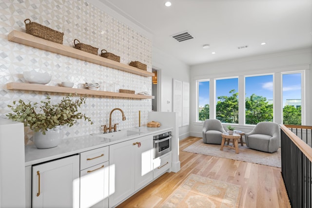 kitchen with open shelves, visible vents, light wood-style flooring, stainless steel oven, and a sink