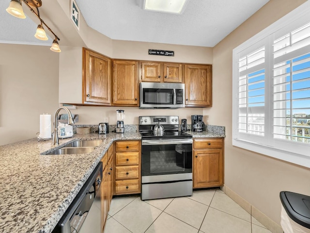 kitchen featuring appliances with stainless steel finishes, brown cabinetry, a sink, and light stone counters