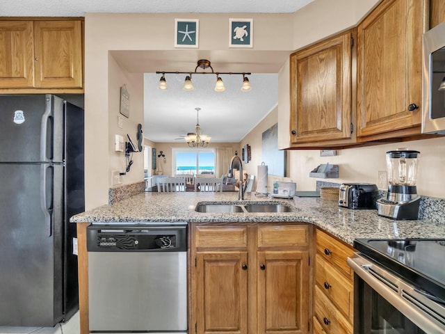 kitchen featuring stainless steel appliances, light stone counters, a sink, and an inviting chandelier