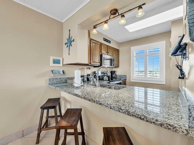 kitchen with brown cabinetry, light stone counters, appliances with stainless steel finishes, a textured ceiling, and a sink