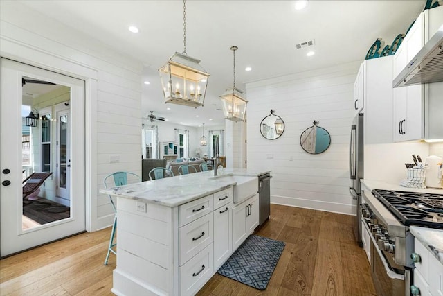 kitchen with wood finished floors, visible vents, appliances with stainless steel finishes, range hood, and a kitchen bar