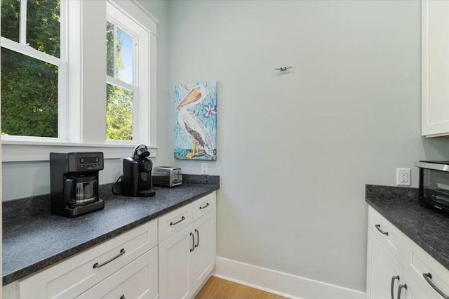 kitchen with light wood-type flooring, a toaster, white cabinets, and baseboards