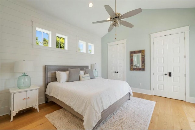 bedroom with light wood-style floors, vaulted ceiling, ceiling fan, and two closets