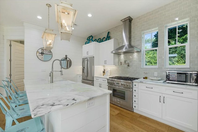 kitchen with light wood finished floors, decorative backsplash, appliances with stainless steel finishes, a sink, and wall chimney range hood