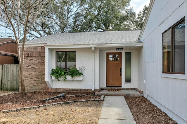 doorway to property featuring fence, brick siding, and a shingled roof