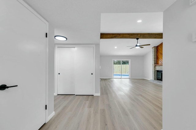 unfurnished living room featuring beamed ceiling, a ceiling fan, a fireplace, light wood finished floors, and baseboards