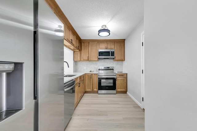 kitchen featuring a sink, light countertops, appliances with stainless steel finishes, a textured ceiling, and backsplash